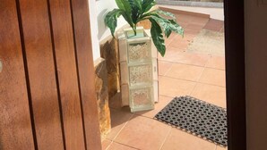 Una puerta que da a un patio con planta en maceta, suelo de baldosas y una reja metálica.