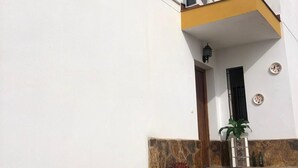Un edificio blanco con un balcón amarillo, base de piedra y escalones que conducen a una puerta.