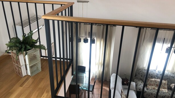 Una escalera con barandillas negras y escalones de madera que conduce a una sala de estar con un sofá y cortinas.