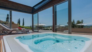 Un área de piscina moderna al aire libre con un jacuzzi, sillas de descanso y un porche acristalado con vistas panorámicas.