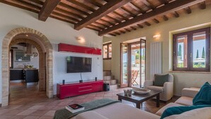 Amplia sala de estar con televisor, mueble de entretenimiento rojo y un rincón de descanso acogedor.