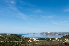 A coastal town with buildings along the shoreline, a clear sky, and a view of the sea and distant islands.