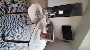A modern dining area with a white table, a patterned rug, a decorative candle holder, and a television on the wall.