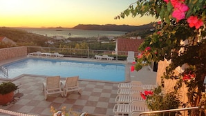 A pool area with chairs and a view of the sea at sunset.