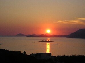 Un coucher de soleil sur une étendue d’eau calme, avec une petite île au centre.