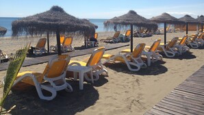 A beach with rows of sun loungers and thatched umbrellas, a wooden walkway, and the ocean in the background.