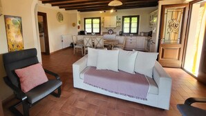 Una sala de estar con un sofá blanco, un sillón negro y una zona de comedor con mesa y sillas de madera.