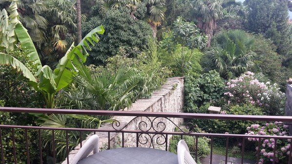 Un balcón con vista a un jardín exuberante, con diversas plantas tropicales y un muro de piedra.