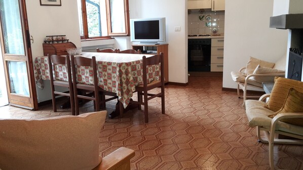 Un coin repas avec une table et des chaises, un téléviseur et, au fond, une cuisine.