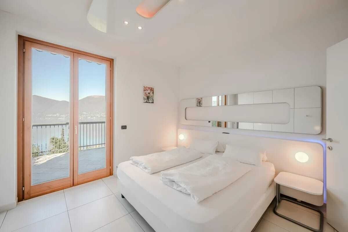Un dormitorio con una cama grande, una puerta corrediza al balcón y una lámpara fijada a la pared.