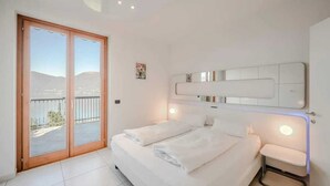Una camera da letto con un letto grande, una porta vetrata scorrevole su un balcone e un lampadario a parete.