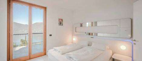 Un dormitorio con una cama grande, una puerta corrediza al balcón y una lámpara fijada a la pared.
