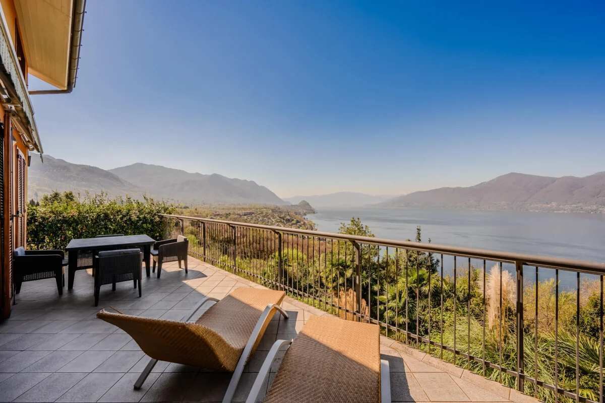 Una terraza con mobiliario exterior, vista a un lago y montañas al fondo.