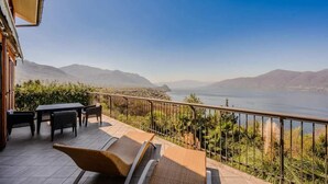 Una terrazza con mobili da esterno, vista su un lago e montagne sullo sfondo.