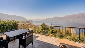 Una terrazza con tavolo e sedie, vista su un lago e montagne.