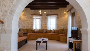 A cozy living room with a stone wall, a wooden bench, a sofa, and a small table with a lamp. - Only 10'min from Rethymno city (Rethymno)