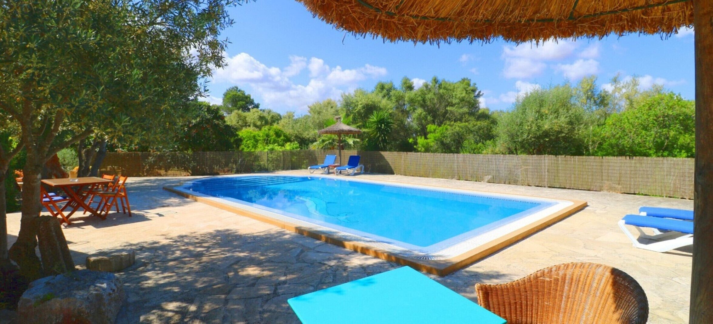 A rectangular swimming pool with a stone deck, surrounded by lounge chairs and a table.