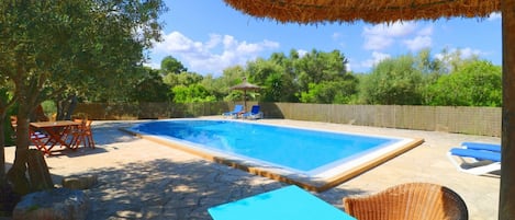 A rectangular swimming pool with a stone deck, surrounded by lounge chairs and a table.