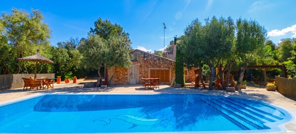 Une piscine avec un bâtiment en pierre et un espace extérieur aménagé pour s’asseoir.