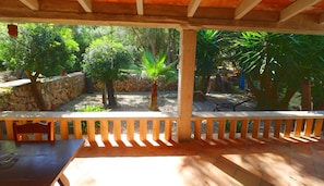 A covered patio area with a table and chairs, surrounded by a stone wall and various trees. - Sa Costa 411 rustic finca with private pool, terrace, garden and air conditioning (Campos)