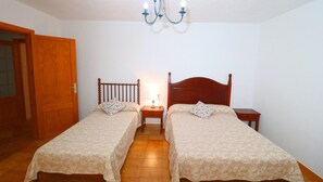 A room with two single beds, wooden headboards, a small bedside table with a lamp, and a wooden door. - Sa Costa 411 rustic finca with private pool, terrace, garden and air conditioning (Campos)