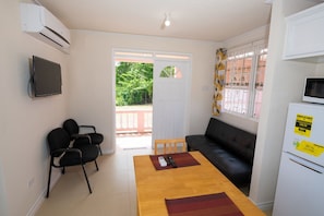 A compact living space with a sofa, a dining table, a TV, and a refrigerator. - THE COTTAGE, SAINT DAVIDS, CHRIST CHURCH, BARBADOS modern 1 bed villa with pool (SAINT DAVIDS)