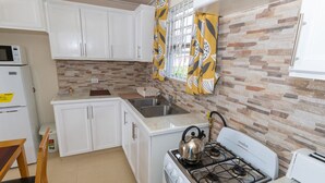 Una cocina compacta con armarios blancos, un microondas integrado, una estufa a gas y un lavabo.