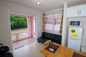 A compact kitchen with a dining area, a sofa, and a refrigerator with a water dispenser. - THE COTTAGE, SAINT DAVIDS, CHRIST CHURCH, BARBADOS modern 1 bed villa with pool (SAINT DAVIDS)