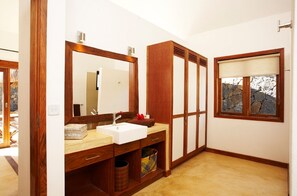 Un baño con tocador de madera, un espejo grande, un lavabo blanco y una ventana con vista a una formación rocosa.