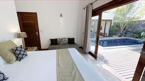 A bedroom with a bed, a nightstand, a lamp, a sofa with cushions, and a sliding glass door leading to a pool area.