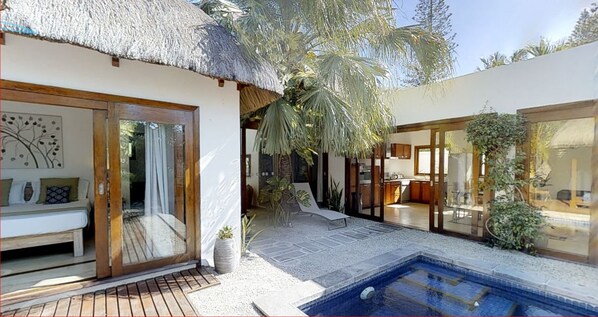 Una villa moderna con entrada de techo de paja, piscina y jardín bien cuidado.