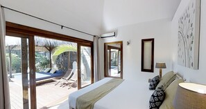 Un dormitorio con cama, ventana, espejo y vista a una piscina y zona de estar exterior.