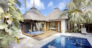 Un resort con dos cabañas de techo de paja, una piscina y plantas tropicales.