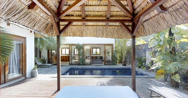 A pool area with a pergola overhead, a covered seating area, and a view of a house with a glass door.