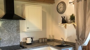 A kitchen with white cabinets, a black stove, a sink, and a clock on the wall. - Cosy dog friendly lodge with Red Squirrels feeding in the garden.outdoor bath (Whitwell)