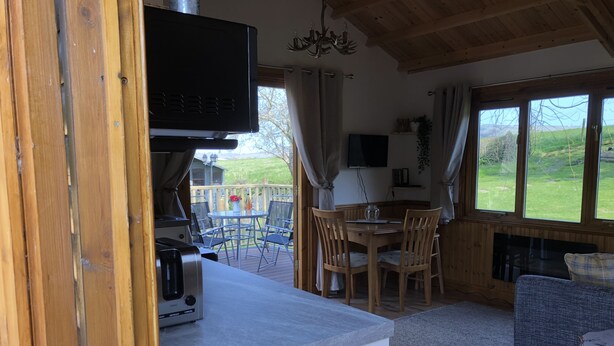 A cozy cabin interior with a wooden dining area, a kitchen with a grill, and a TV mounted above the counter. - Cosy dog friendly lodge with Red Squirrels feeding in the garden.outdoor bath (Whitwell)