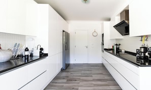 Une cuisine moderne avec des meubles blancs, un plan de travail noir, un réfrigérateur en acier inoxydable et une machine à café.