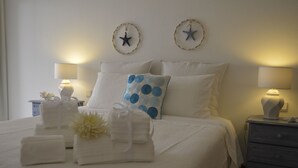 Ein ordentlich bezogenes Bett mit weißen Leinen, einem blau gepunkteten Kissen und dekorativen Wandbildern mit Sternenmotiven.
