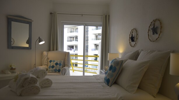 Ein Hotelzimmer mit einem Bett, einem Sessel, einem Schreibtisch und einem Fenster mit Blick auf Gebäude.