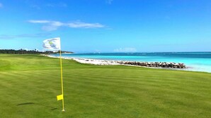A golf course with a flag on a flagstick, a clear blue sky, and a view of the ocean.