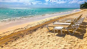 A beach with white lounge chairs and a clear view of the ocean.