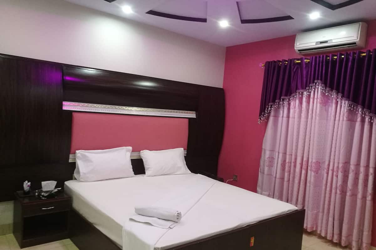 Una habitación de hotel con cama, mesita de noche y unidad de aire acondicionado.