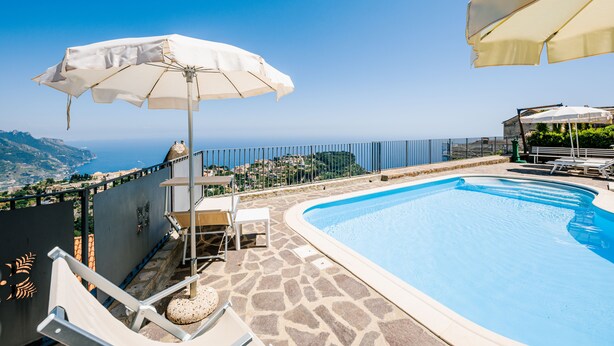 A swimming pool with a view of the sea, surrounded by lounge chairs and umbrellas.