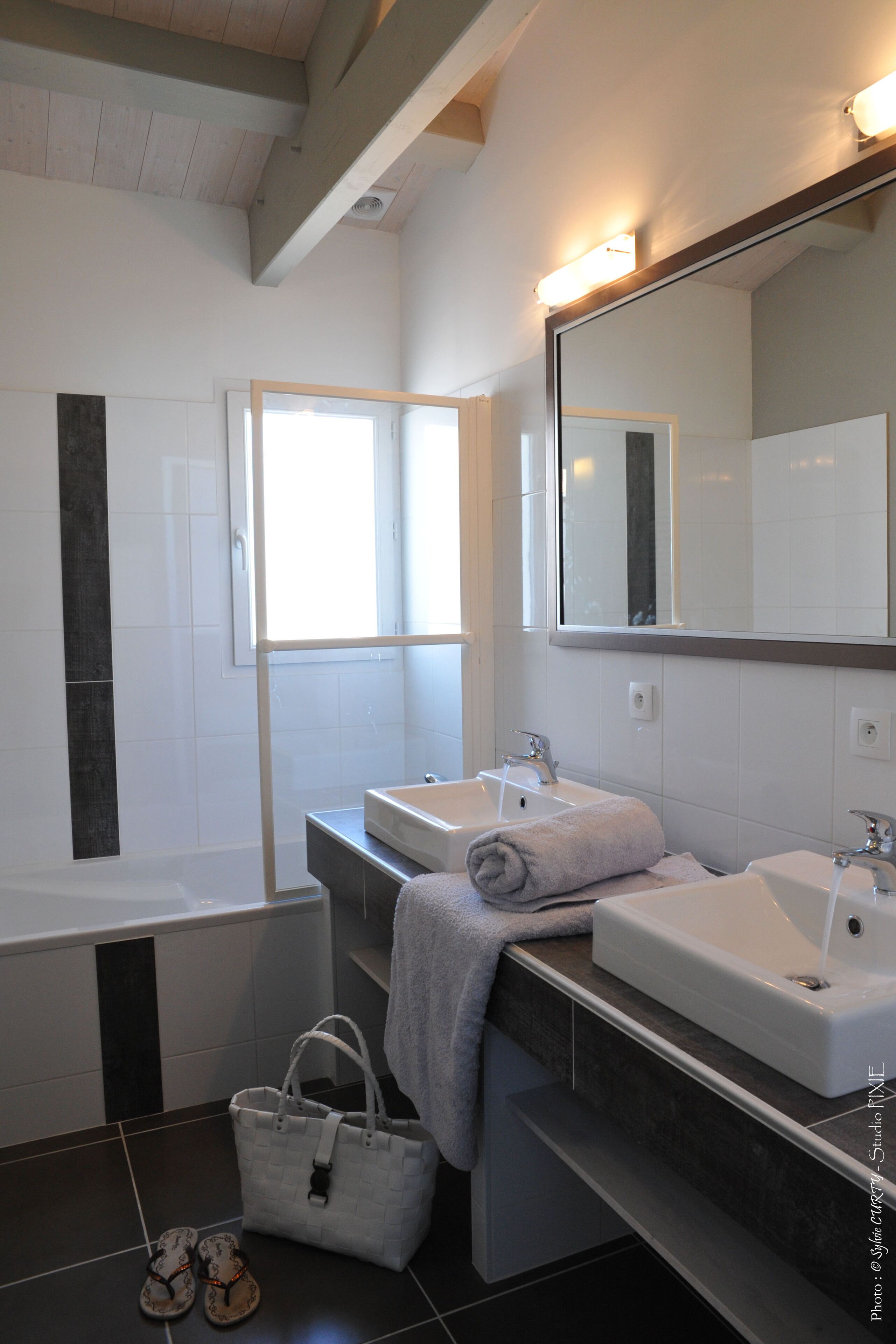 Un baño moderno con bañera, dos lavamanos, un espejo grande y una ventana.