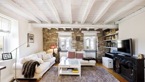 A living room with a stone wall, white furniture, a fireplace, and a television. - Big traditional basque villa with  enclosed garden (Ascain)