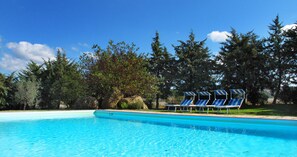 En klar, blå swimmingpool med liggestole og udsigt til træer og klipper.