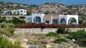 A modern villa with multiple white structures, stone walls, and red flowering plants. - AELIA LUXURY VILLA IN A PRIVATE ESTATE IN ARDANI KARPATHOS (Amoopi)
