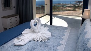 A hotel room with a bed, a dresser, a mirror, and a view of the sea and a bridge. - AELIA LUXURY VILLA IN A PRIVATE ESTATE IN ARDANI KARPATHOS (Amoopi)