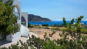 A modern building with a white exterior and a clear view of the sea and a distant hill. - AELIA LUXURY VILLA IN A PRIVATE ESTATE IN ARDANI KARPATHOS (Amoopi)
