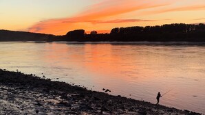 Une rivière au coucher du soleil, avec une personne qui pêche.